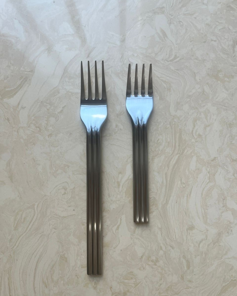 Two silver forks on a textured beige surface